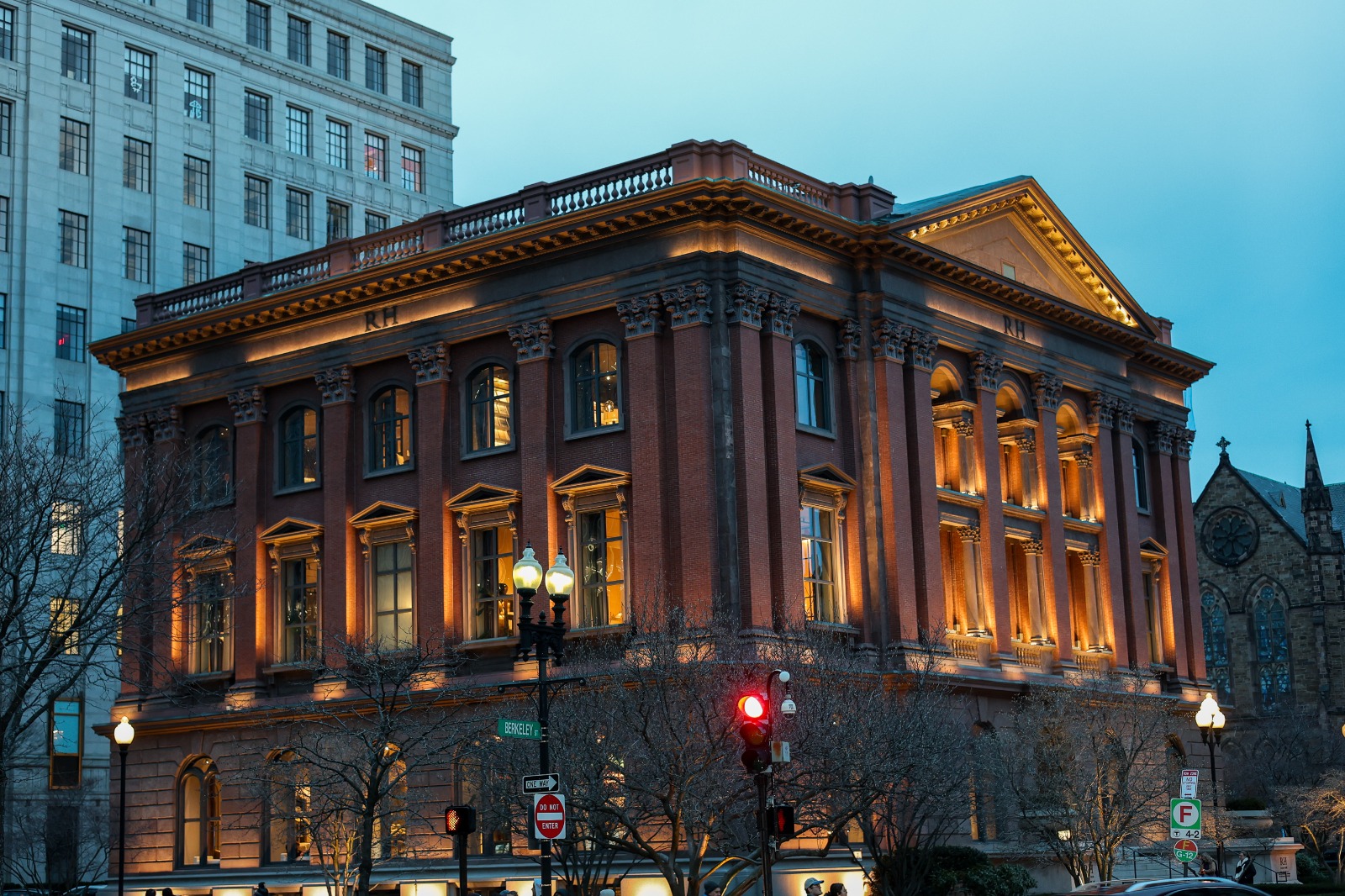 A grand, historic brick building with Classical columns and warm uplighting, captured at twilight on a city street corner in Boston.